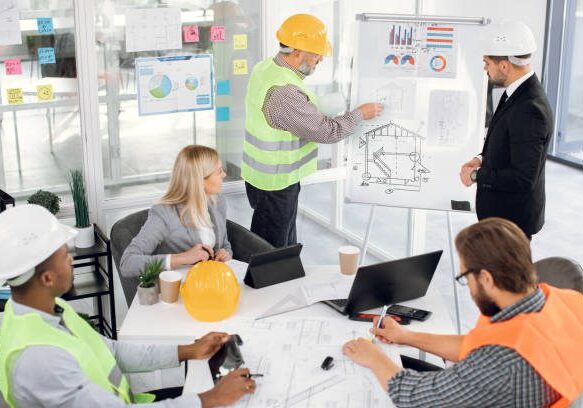 Focused bearded male chief in suit listening to professional middle aged bearded man builder contractor about building plan on blueprint from during meeting in boardroom